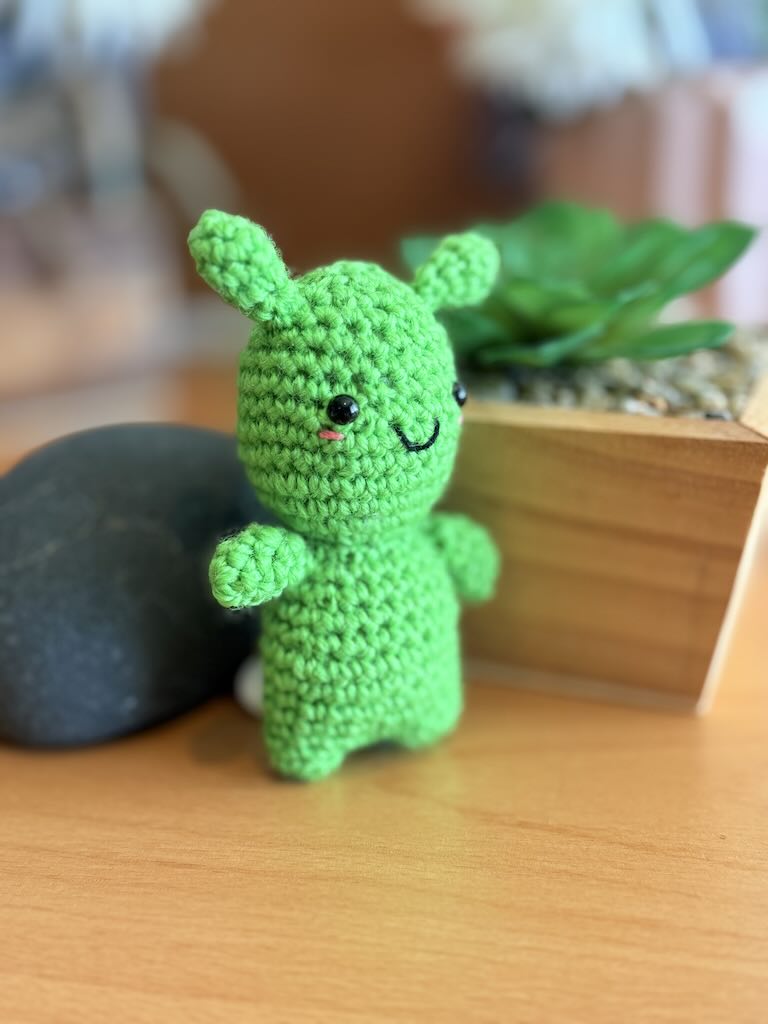 handmade crochet green alien toy with small eyes and cheerful smile