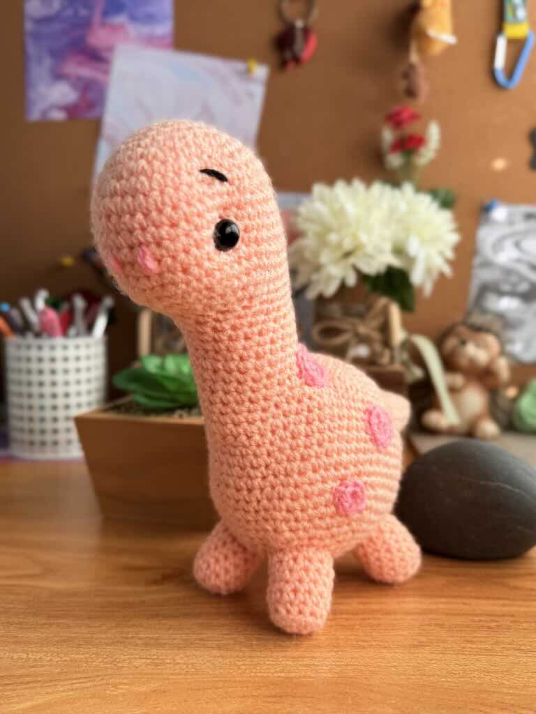handmade crochet pink baby brontosaurus toy with long neck and gentle expression