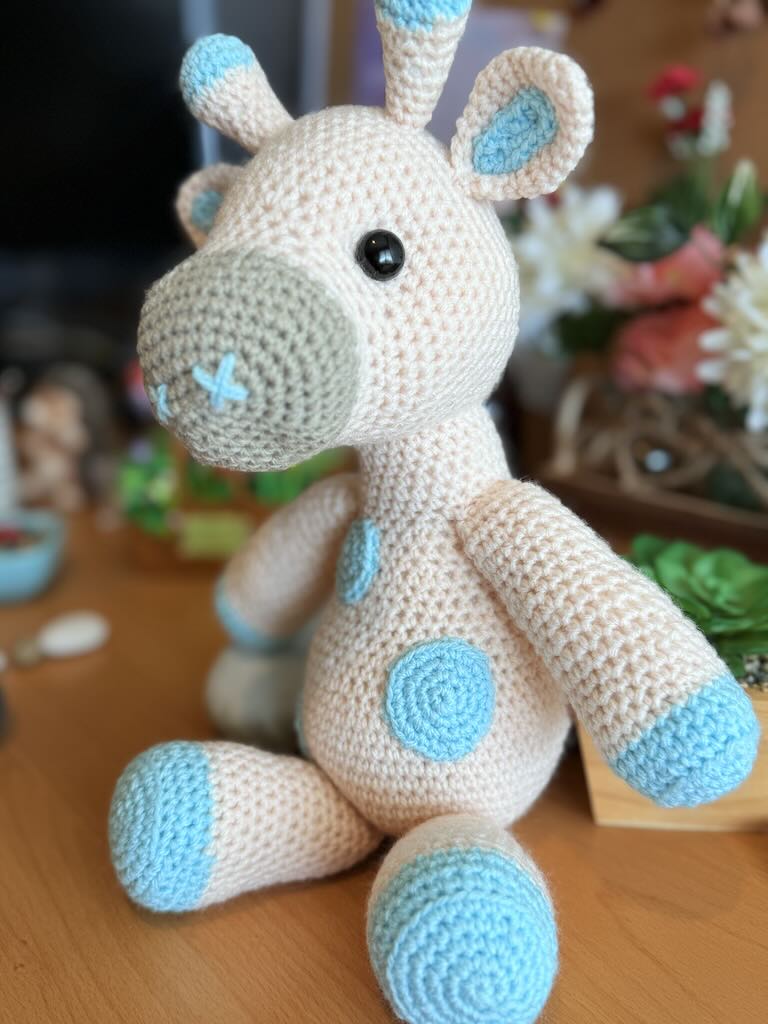 handmade crochet giraffe toy named Ginny with long neck and cream body with blue dots